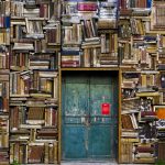 Wall Covered in Books with Small Blue Door in the middle